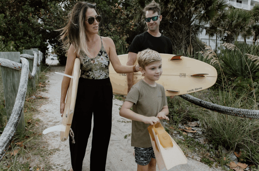 Family walking to the beach with surfboards and fins near Private Homes vacation rentals in Florida.